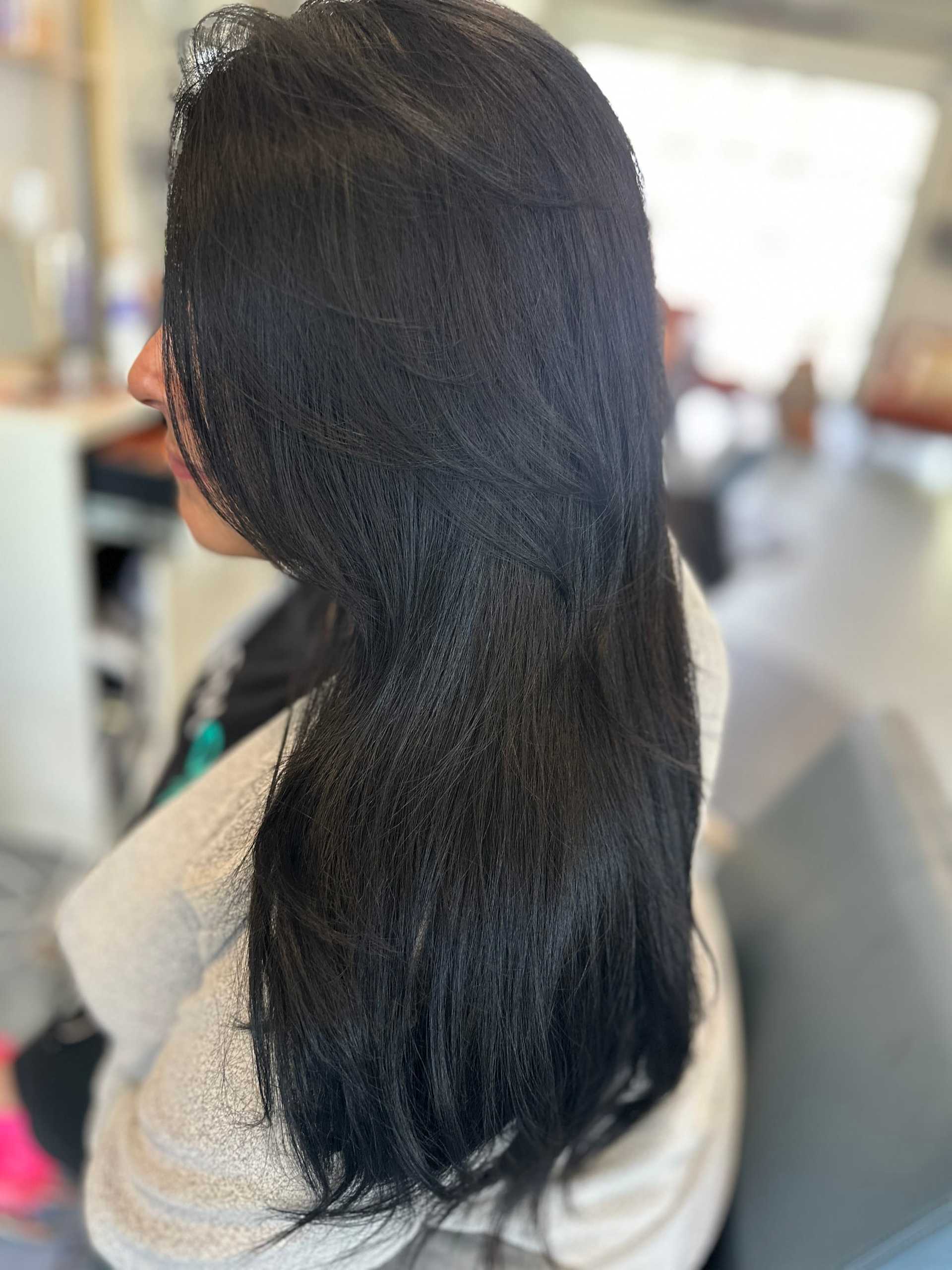 Long, sleek black hair styled smoothly, captured from the side in a bright salon setting.