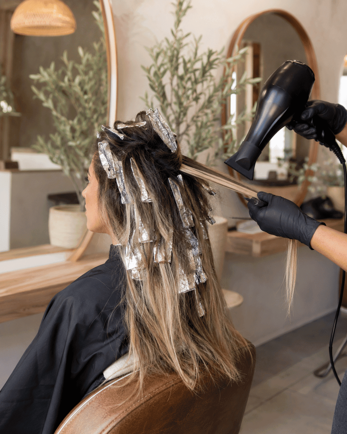 Hair stylist blow-drying client's hair with foils in a salon setting.